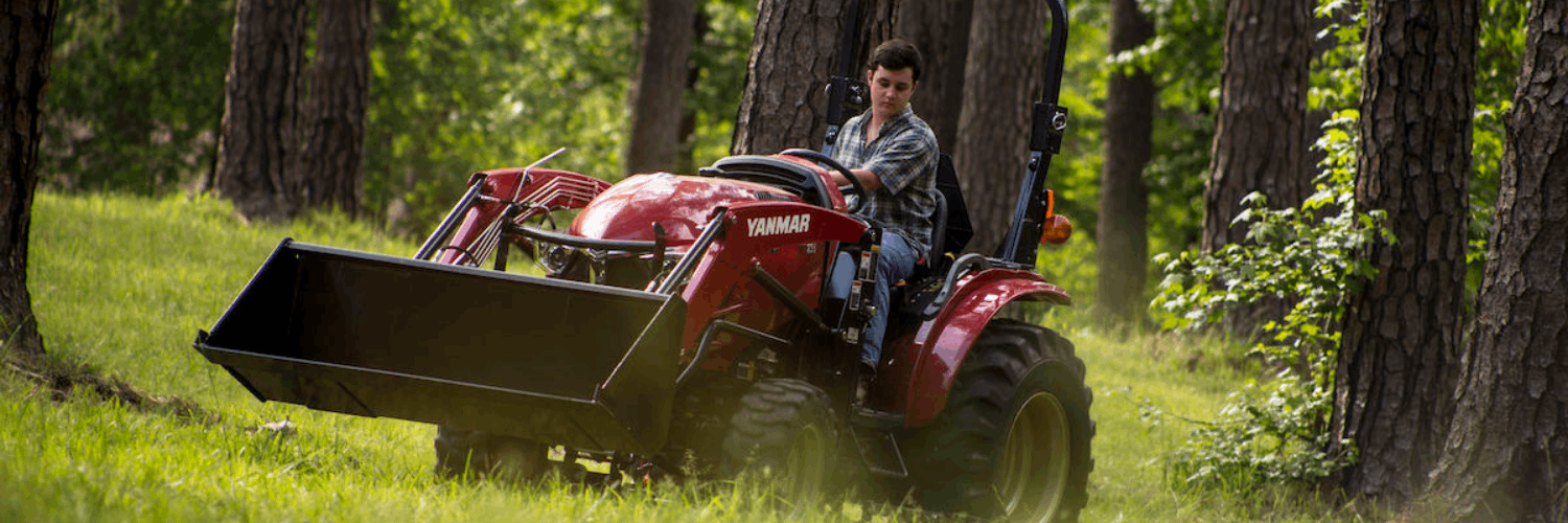 Image of person riding a Yanmar tractor in a wooded area.